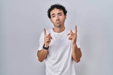 Hispanik adam arka planda dikiliyor üzgün ve üzgün görünüyor, parmaklarıyla yön gösteriyor, mutsuz ve depresif.. 