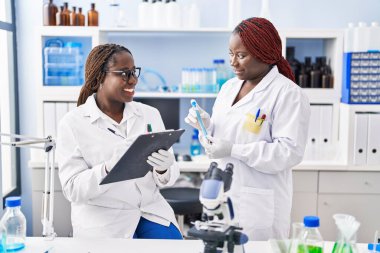 African american women scientist holding test tube writing on document at laboratory