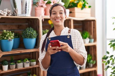 Çiçekçiye akıllı telefon kullanarak gülümseyen güzel İspanyol kadın.