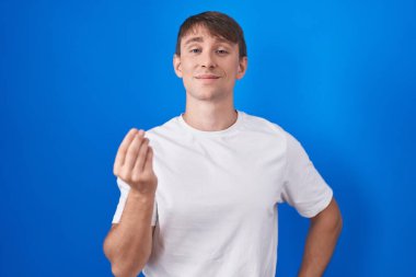 Kafkasyalı sarışın adam mavi arka planda duruyor. İtalyan jestleri yapıyor. Elleri ve parmakları kendinden emin. 