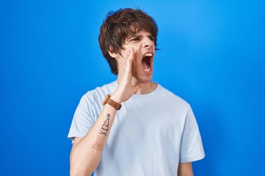 Latin kökenli genç adam mavi arka planda durup el ele tutuşarak bağırıyor ve çığlık atıyordu. iletişim konsepti. 