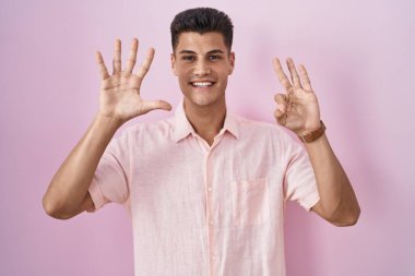 Pembe arka planda dikilen genç İspanyol adam 8 numaralı parmaklarıyla gülümseyerek kendinden emin ve mutlu bir şekilde işaret ediyor.. 