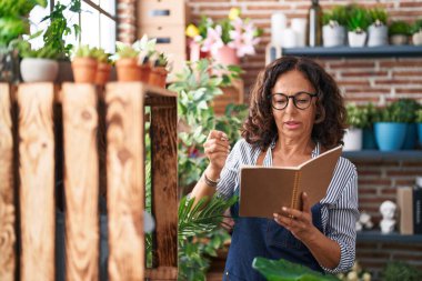 Middle age woman florist writing on notebook at flower shop