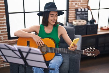 Genç İspanyol kadın müzisyen müzik stüdyosunda klasik gitar çalmak için akıllı telefon kullanıyor.