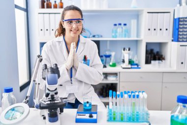 Laboratuvarda çalışan Latin kökenli genç bir kadın ellerini birleştirip af diliyor kendinden emin bir şekilde gülümseyerek.. 