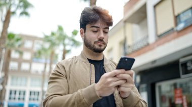 Genç İspanyol adam akıllı telefon kullanıyor. Sokakta ciddi bir ifadesi var.