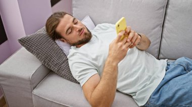 Evdeki kanepede uzanmış akıllı telefon kullanan genç bir İspanyol.