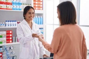 Two women pharmacist and customer holding pills bottle at pharmacy