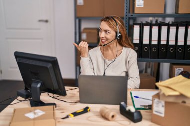 Küçük işletme şirketinde çalışan İspanyol bir kadın. Kulaklık takıyor, baş parmağıyla yan tarafa bakıyor ve ağzı açık gülümsüyor. 