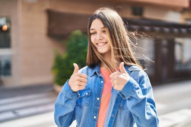 Adorable girl smiling confident doing ok sign with thumbs up at street