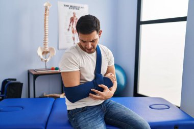 Young hispanic man injured physiotherapy patient suffering for arm pain at rehab clinic