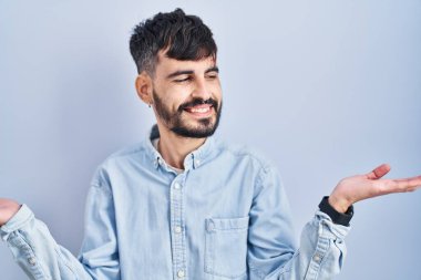 Mavi arka planda duran sakallı genç İspanyol adam gülümseyerek iki elini de açık tutuyor, sunuyor ve reklam karşılaştırması yapıyor ve dengeyi sağlıyor. 