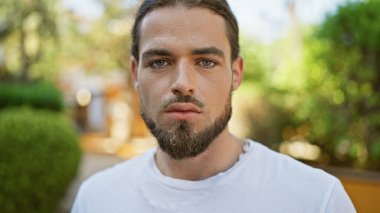 Young hispanic man standing  with serious expression at park