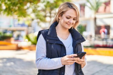 Parkta akıllı telefon kullanan, kendine güvenen genç sarışın kadın.