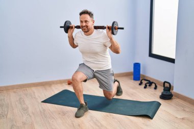 Young caucasian man smiling confident training legs exercise at sport center