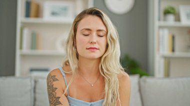 Kanepede oturan, gözleri kapalı genç sarışın kadın.