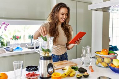 Genç, güzel, İspanyol bir kadın blender ile smoothie hazırlıyor. Mutfaktaki tabletten tarifine bakıyor.