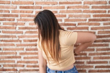 Genç esmer kadın tuğlaların başında duruyor sırt ağrısı çekiyor, elleriyle dokunuyor, kas ağrısı çekiyor. 