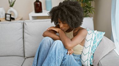 Afro-Amerikalı kadın ciddi bir yüzle kanepede oturuyor.