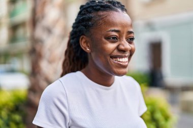 Afro-Amerikalı kadın gülümsüyor. Kendinden emin bir şekilde caddeye bakıyor.