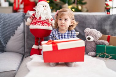 Sevimli İspanyol kız elinde hediyeyle evdeki Noel ağacının yanındaki koltukta oturuyor.