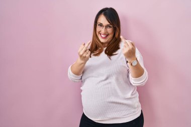 Pregnant woman standing over pink background showing middle finger doing fuck you bad expression, provocation and rude attitude. screaming excited 