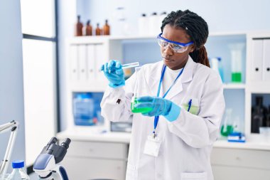 Laboratuvarda test tüpüne sıvı döken Afrikalı Amerikalı kadın bilim adamı.