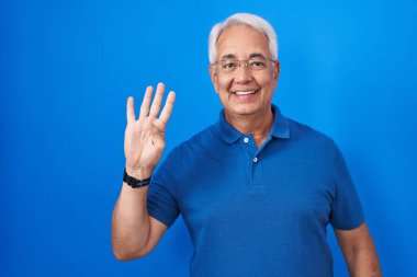 Middle age man with grey hair standing over blue background showing and pointing up with fingers number four while smiling confident and happy. 