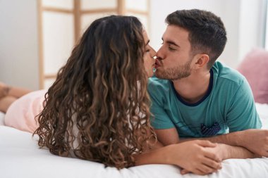 Yatakta uzanmış yatak odasında öpüşen genç İspanyol çift.