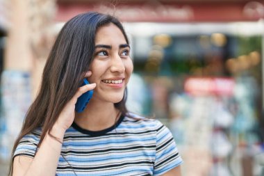 Young hispanic girl smiling confident talking on the smartphone at street