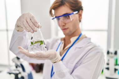 Young caucasian man scientist holding test tube with plant at laboratory