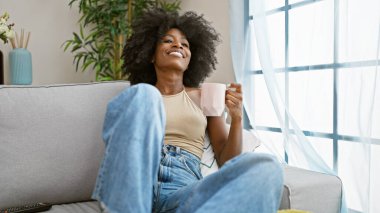 African american woman drinking coffee sitting on sofa at home