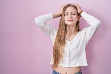 Young caucasian woman standing over pink background suffering from headache desperate and stressed because pain and migraine. hands on head. 