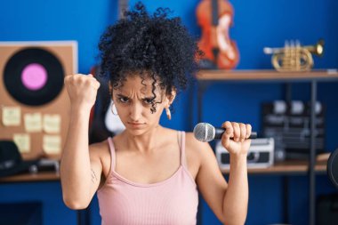 Müzik stüdyosunda mikrofon kullanarak şarkı söyleyen kıvırcık saçlı İspanyol kadın öfkeyle bağırıyor, öfkeyle bağırıyor ve el kaldırıyor. 