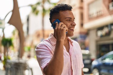 Genç Latin adam gülümsüyor. Kendine güveniyor. Akıllı telefondan konuşuyor.