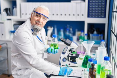 Middle age grey-haired man scientist writing on document holding bottle at laboratory
