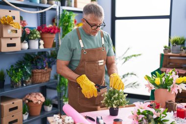 Middle age grey-haired man florist cutting plant at flower shop