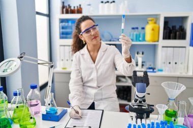 Genç ve güzel İspanyol bilim kadını. Laboratuvarda elinde test tüpü olan bir belgeye yazı yazıyor.