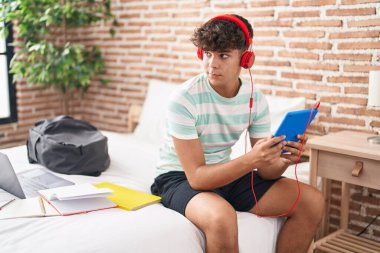 Young hispanic teenager student sitting on bed studying at bedroom