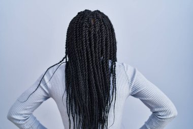 Mavi arka planda dikilen Afrikalı Amerikalı kadın geriye bakıyor kolları vücudunda. 