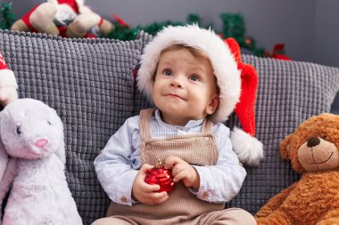 Sevimli sarışın bebek koltukta oturuyor. Evde Noel şapkası takıyor.