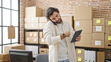 Latin kökenli genç bir iş adamı ofisteki telefonda konuşurken touchpad kullanıyor.