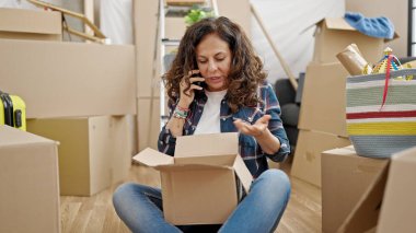 Orta yaşlı İspanyol kadın telefonda konuşuyor. Yeni evdeki karton kutuları açıyor.