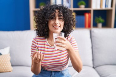 Orta doğulu genç bir kadın evdeki kanepede oturmuş hap alıyor.