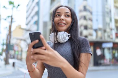 Young arab woman smiling confident using smartphone at street