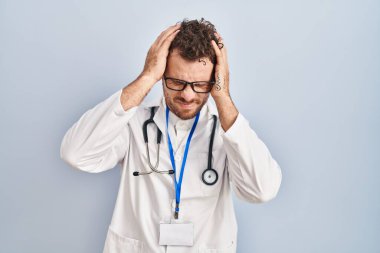 Doktor üniforması giyen genç İspanyol bir adam ve steteskop. Ağrı ve migren yüzünden çaresiz ve stresli baş ağrısı çekiyor. Eller başının üstünde.. 