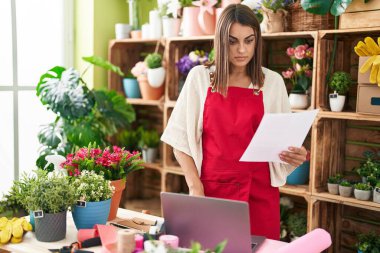 Young beautiful hispanic woman florist using laptop reading document at flower shop