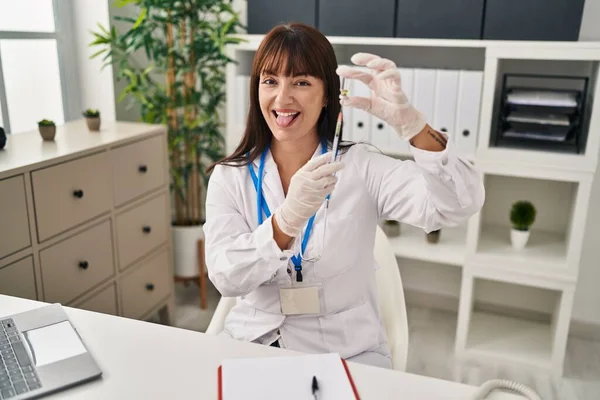 Młoda Brunetka Lekarz Kobieta Trzyma Strzykawkę Szczepionkę Wystający Język Szczęśliwy — Zdjęcie stockowe