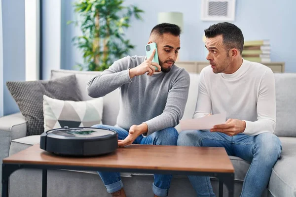 Two men talking on smartphone with technician vacuum robot service at home
