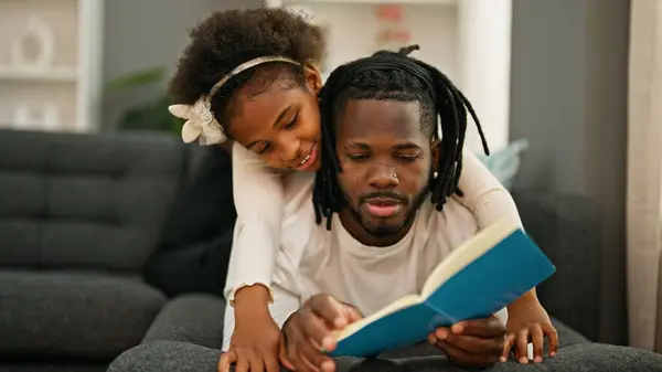 アフリカ系アメリカ人の父親と娘が自宅でソファーの読書本に横たわる — ストック写真